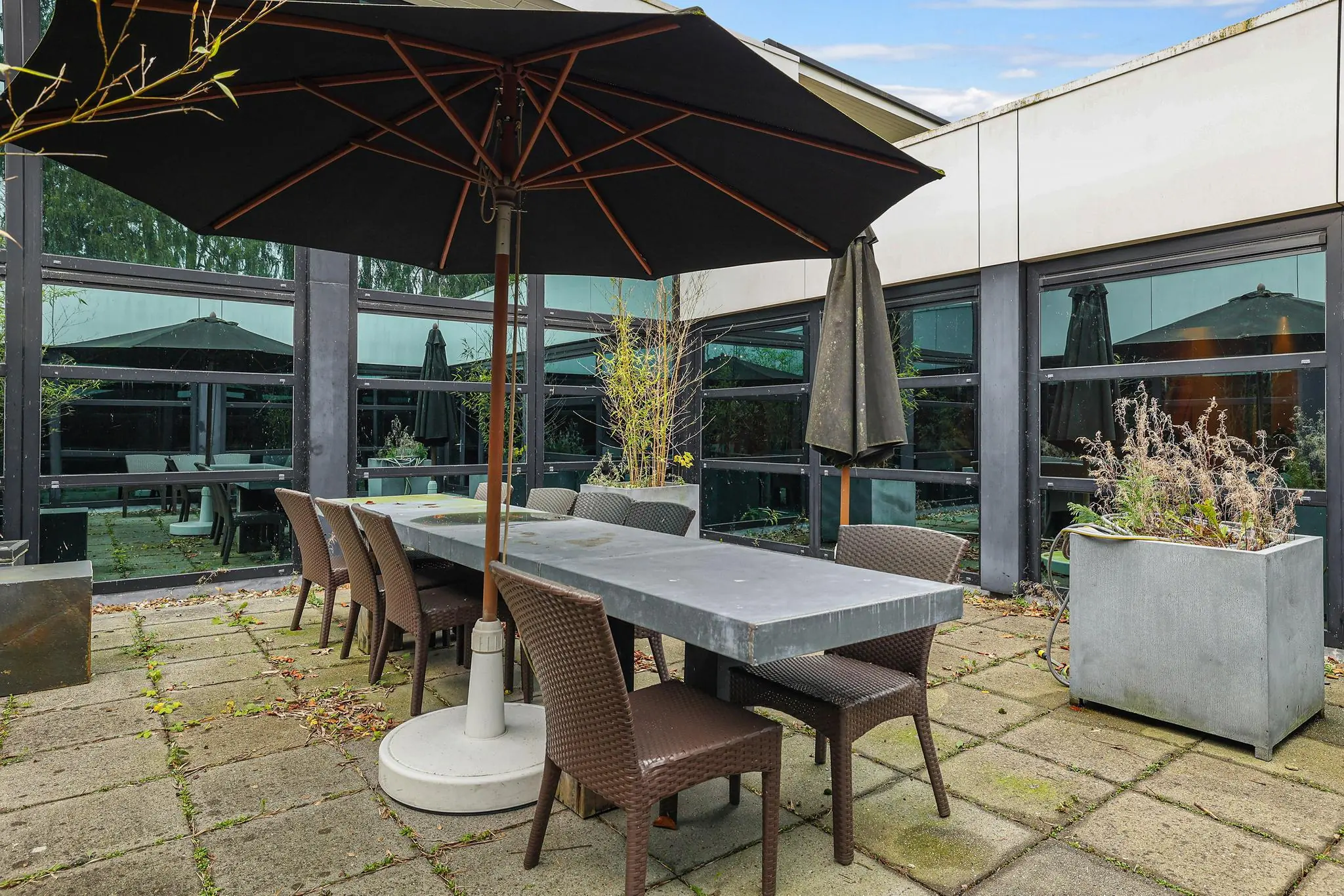 Binnenplaats met een lange buitentafel, stoelen en een grote zwarte parasol aan de Oude Utrechtseweg.